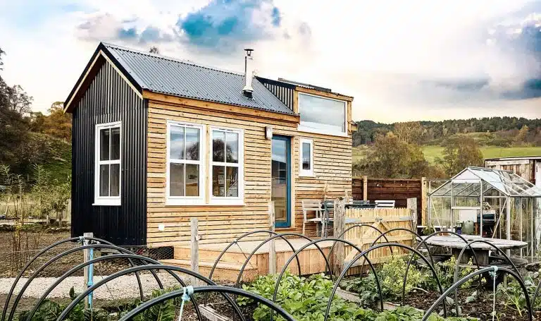 Modern tiny house with wood and metal exterior nestled in a rural Aberdeenshire setting, surrounded by vegetable gardens and a greenhouse showcasing sustainable tourism and eco-friendly living in the Scottish countryside.